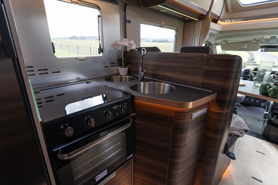 4-berth campervan kitchen with gas cooker, oven, sink and countryside view