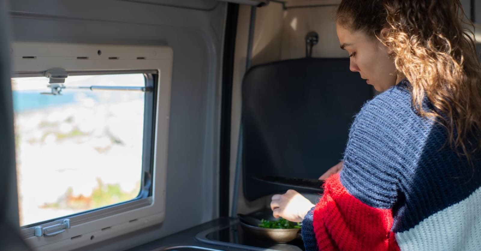 Preparing food inside a campervan with a scenic view outside