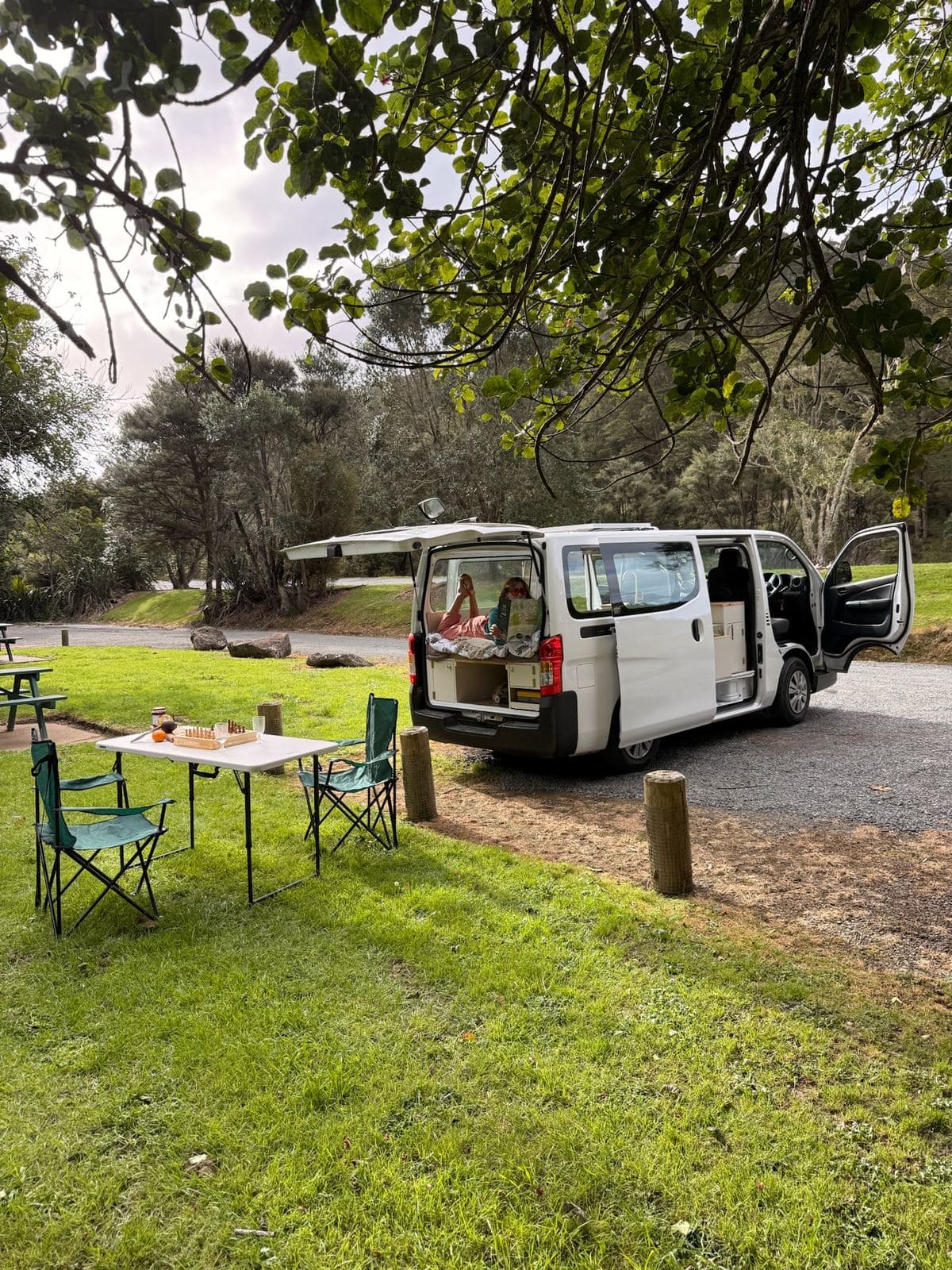 Pīwakawaka campervan at a New Zealand campsite with the camp table and chairs set up on the grass