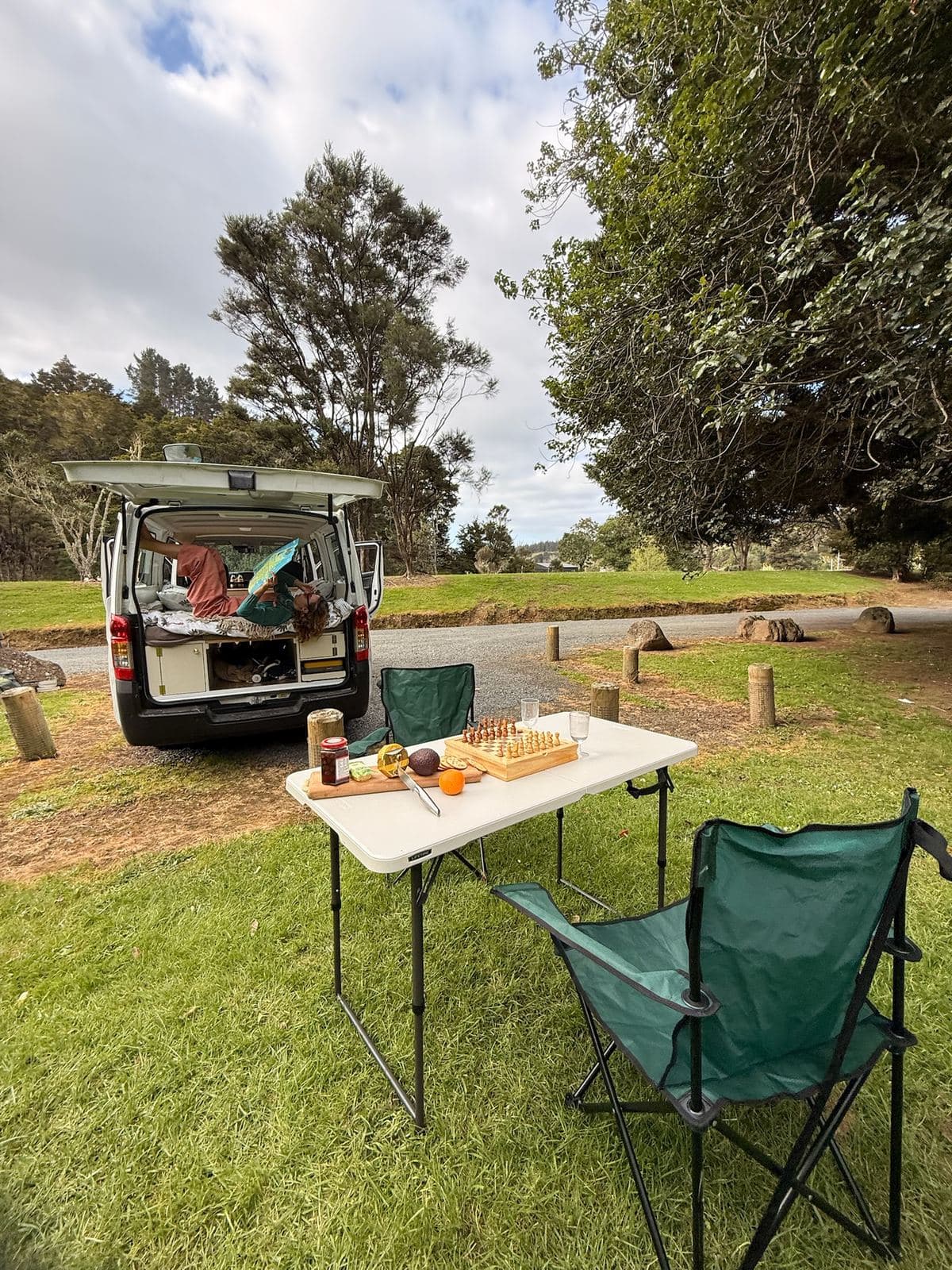 The Pīwakawaka at a grassy New Zealand campsite with the camp table, chairs and a chess set out