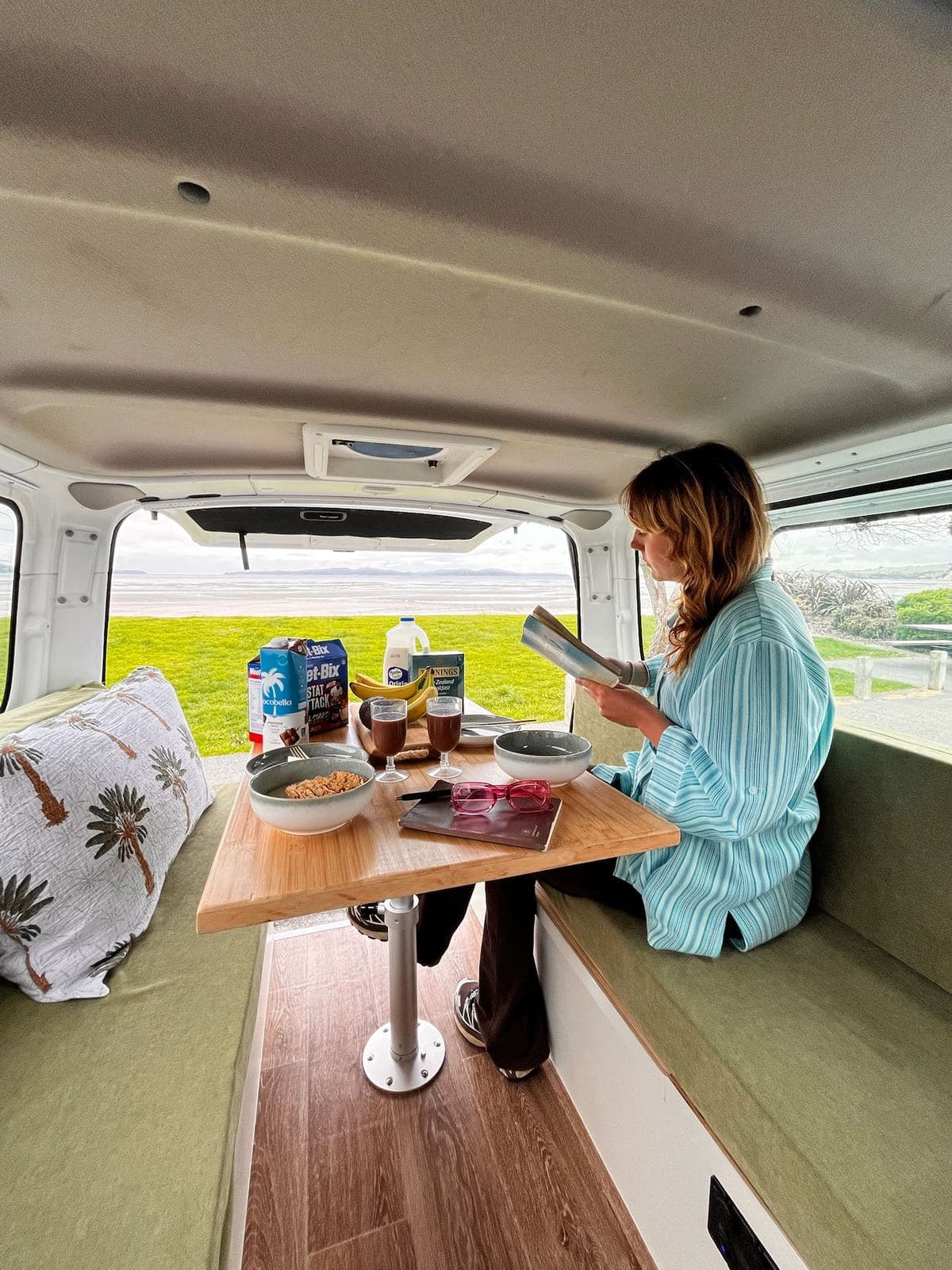 The Pīwakawaka's dinette table set for breakfast with the rear doors open to an estuary