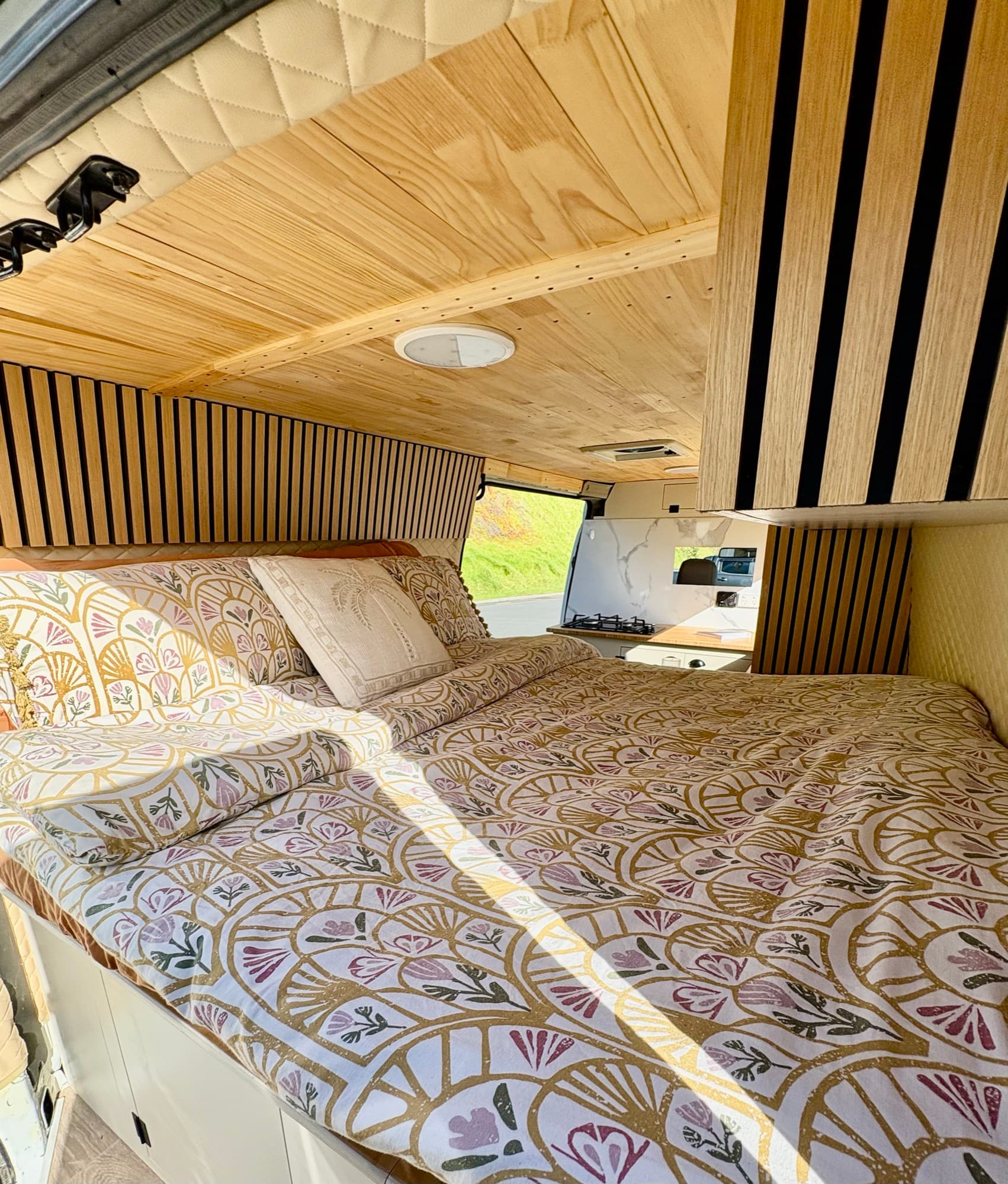 Tūī 2-berth campervan double bed made up with patterned bedding under a wood-panelled ceiling