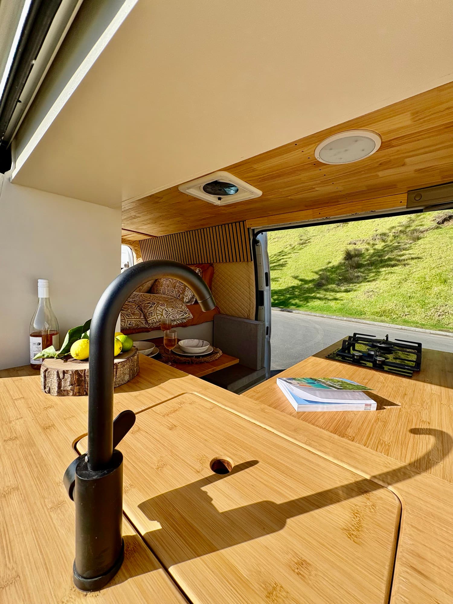Tūī 2-berth campervan dinette with the sliding side door open to New Zealand hills