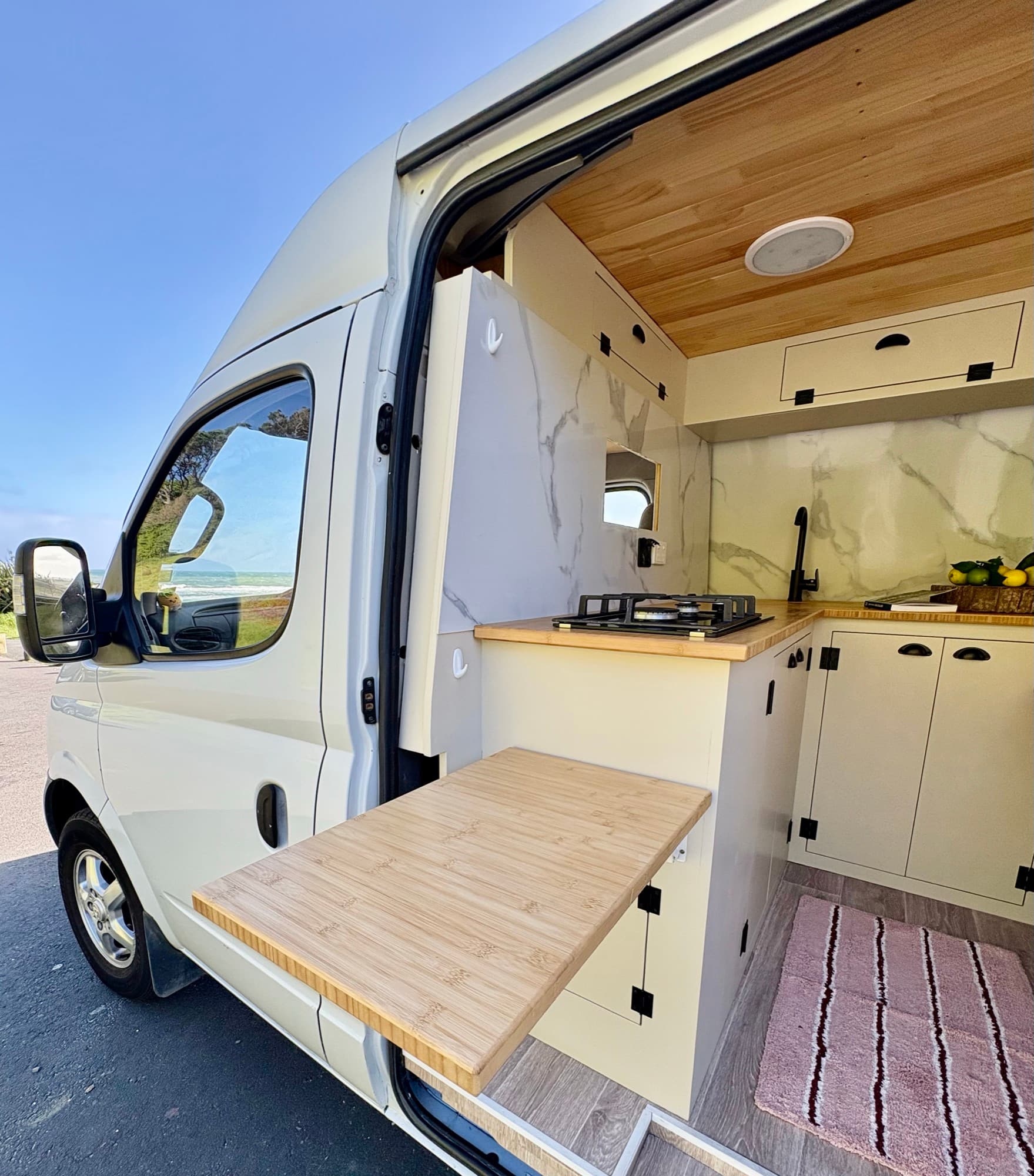 Tūī 2-berth compact self-contained campervan parked at a New Zealand beach with the side door open