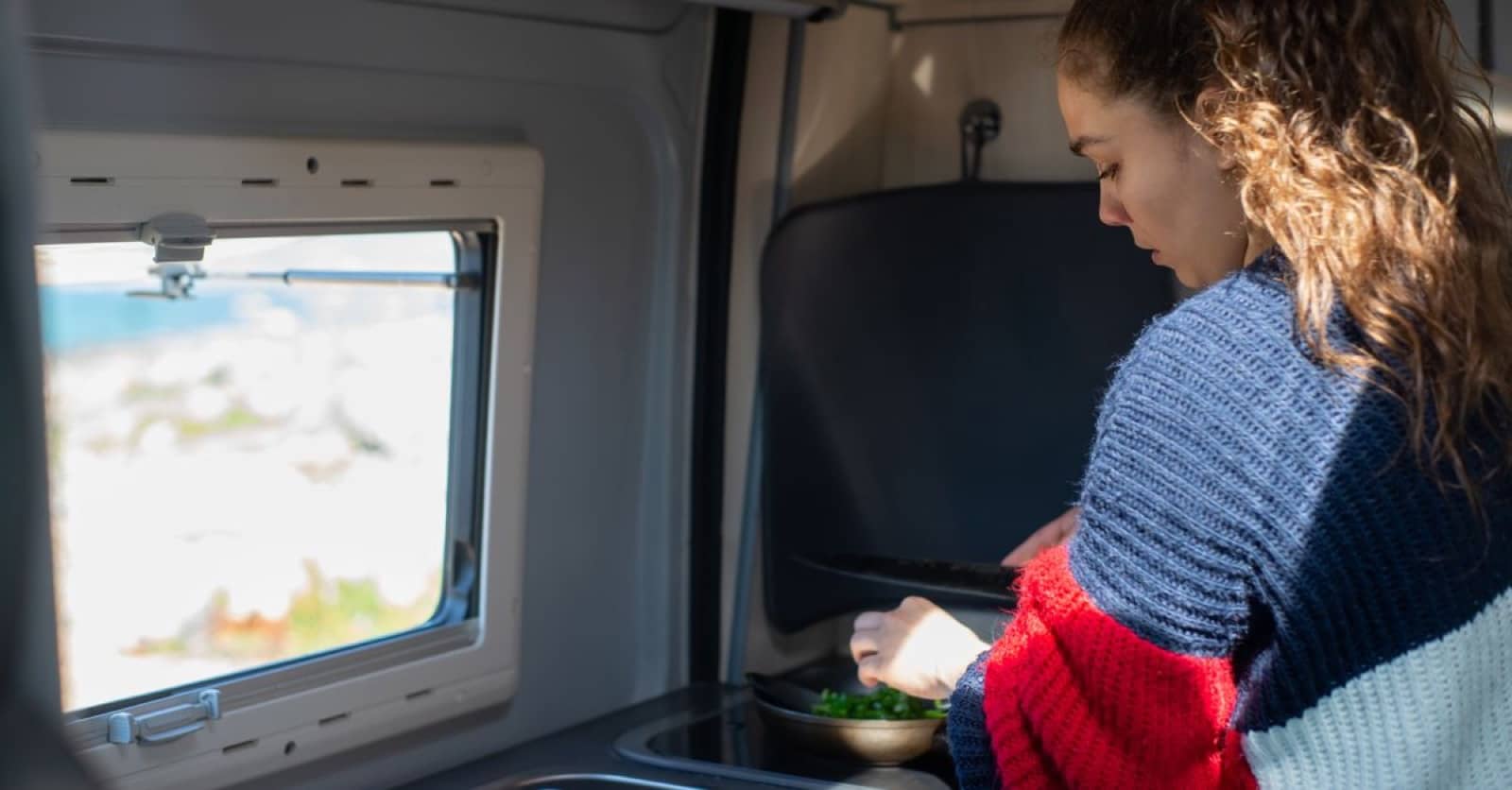 Preparing food inside a campervan with a scenic view outside