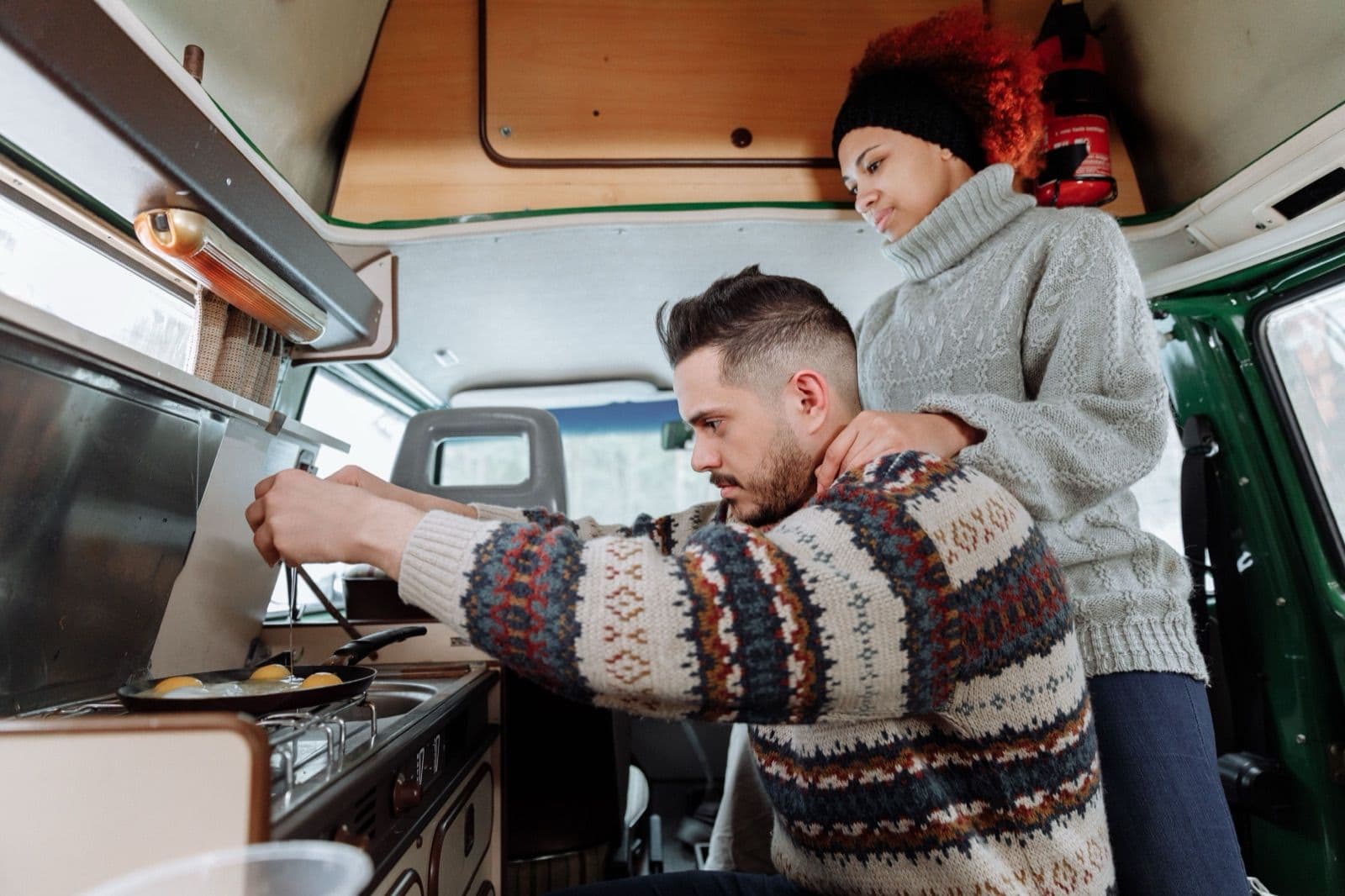 Couple cooking inside a compact campervan, where the seating area doubles as the living space