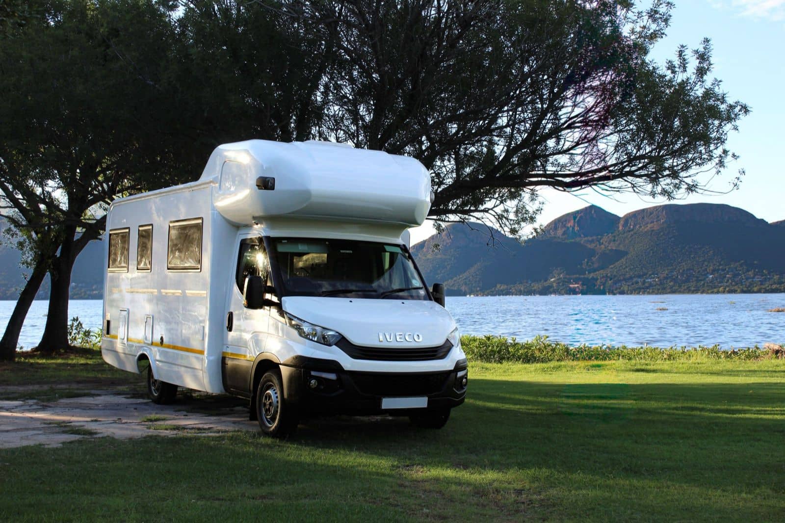Coachbuilt motorhome parked on grass beside the water, noticeably larger than a compact campervan