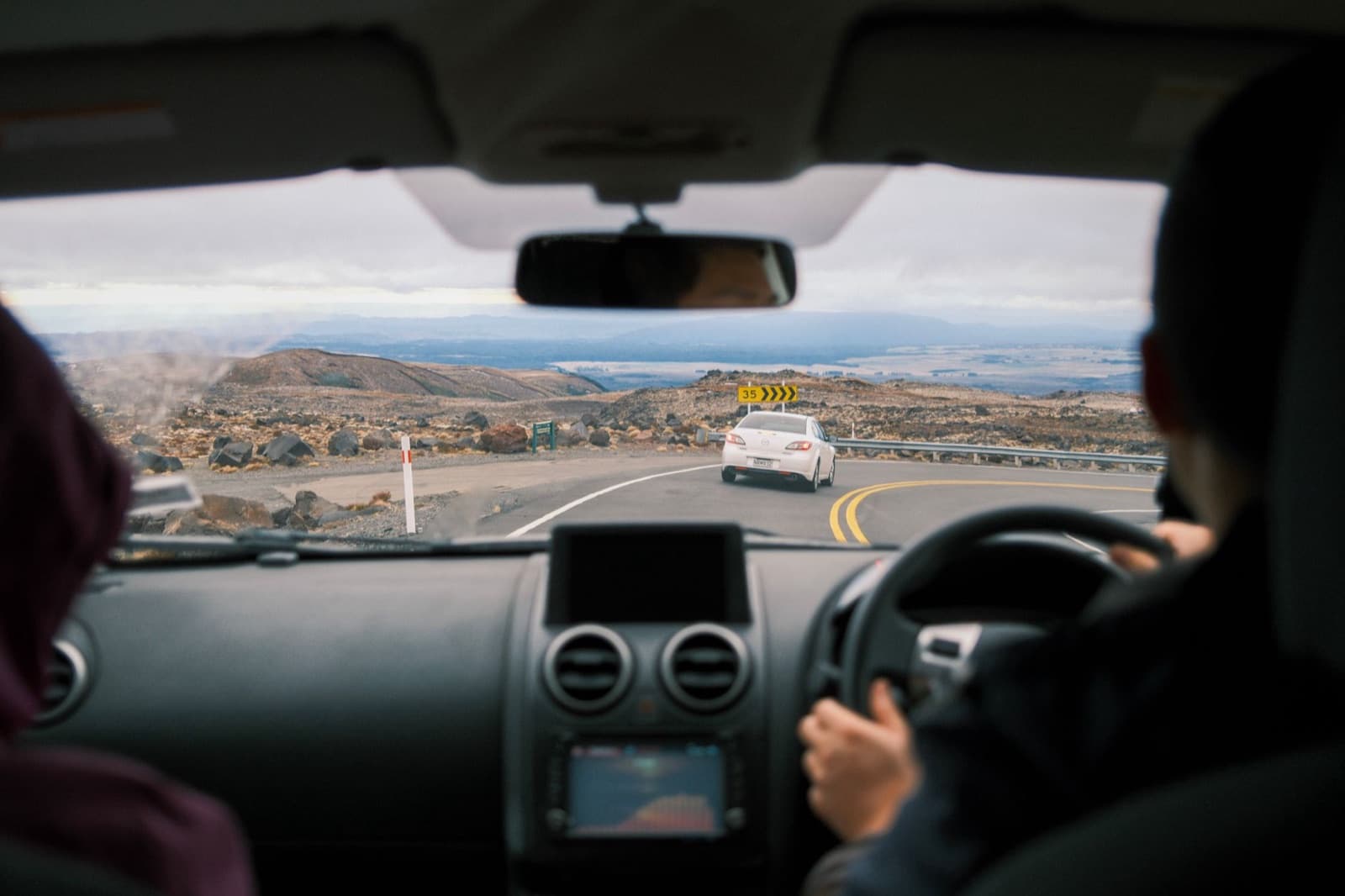 View through the windscreen of a rental car following another car on a winding New Zealand mountain road