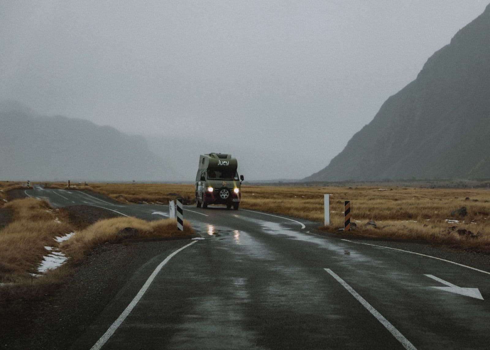 Open road curving through a valley in New Zealand, with a campervan in the distance