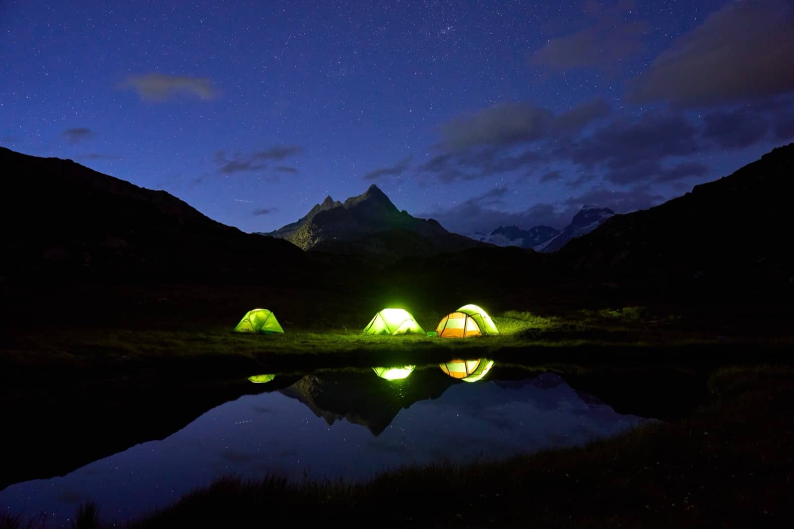 Tent glowing at night beside a mountain lake while freedom camping in New Zealand
