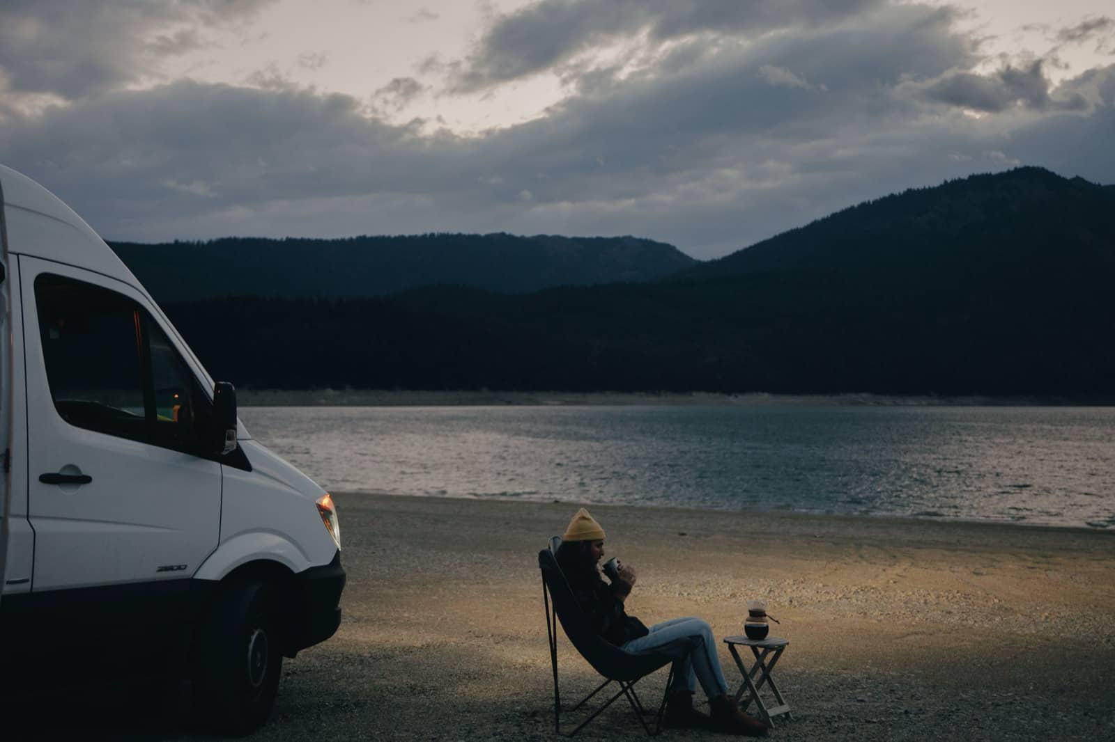 Unmarked campervan and a camp chair beside a lake at dusk, the kind of quiet spot New Zealand freedom campers look for